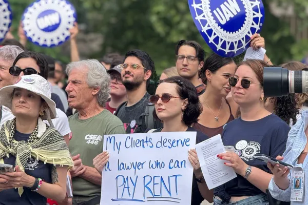 ALAA member at rally holding sign that says "my clients deserve a lawyer who can pay rent"