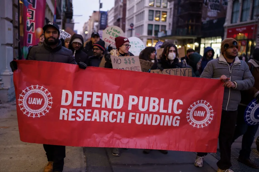 UAW members holding sign that says "defend public research funding"